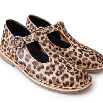 A pair of T-bar Mary Jane style shoes featuring a bold leopard print on a white background. The shoes have a silver-tone buckle closure on the strap and decorative teardrop-shaped cutouts on the toe area forming a floral design. The soles are light brown with visible white stitching along the edge.