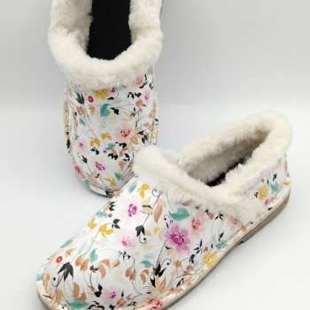 A pair of white slip-on slippers with a multi-colored floral print, known as the Jo Printed Vellie Slipper, shown on a white background. The slippers feature a thick, white fluffy lining around the opening and a low-profile tan sole with visible stitching. One slipper is angled in the foreground while the other stands vertically behind it.