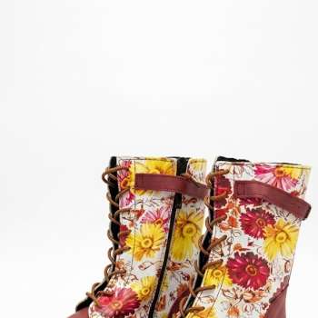 A pair of mid-calf lace-up boots featuring the "Millie Print," displayed on a white background. The boots have a smooth burgundy leather toe and heel, while the sides and shaft are covered in a vibrant yellow and pink floral pattern. They include brown laces, a burgundy buckle strap at the top, and a side zipper.